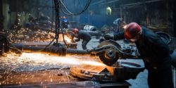 Photo: A person wearing a safety helmet and protective gloves welds steel with a circular saw, spraying sparks, in a factory; Copyright: envato/romankosolapov